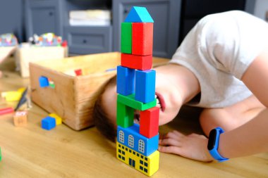 Küçük çocuk, çocuk renkli ahşap figürlerden kuleler ve binalar inşa ediyor, konut inşaatı konsepti, mortgage, sigorta, mutlu çocukluk, çocuk oyunları