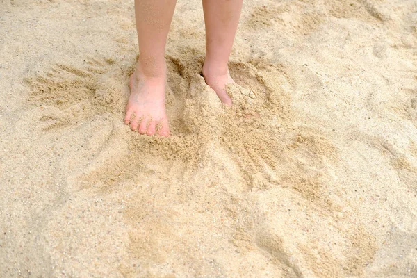 child\'s bare feet in the sand, boy plays in the summer with sand on the playground, in the sandbox, the concept of building sand castles, summer vacation, fun on the beach