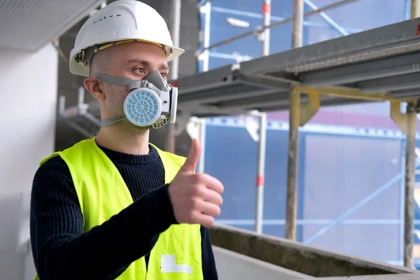 young male builder foreman, worker or architect in white hardhat and protective respirator during inspection in construction site, concept of monitoring repair of buildings, structures