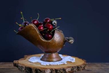 Güzel olgun kiraz, küçük bir damla suda koyu mavi bir zemin üzerinde eski bir bakır kül kapında mevsimlik meyve, meyve, sıcak yaz mevsiminde tazelik, susuzluk giderme, yaz mevsimi