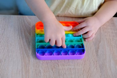 Gökkuşağı oyuncağı anti-stresi Patlat onu, küçük çocuk, 2 yaşında bir kız parmaklarıyla bastırıyor baloncukları, anti-stres cihazıyla oynuyor psikolojik rahatlama için