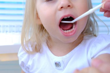 Kapalı kadın elleri, dişçi, doktor küçük bir hastanın ağız boşluğunu muayene ediyor. Sarışın kız 2 yaşında, azı dişi büyümüş, ağzı açık çocuk, çocuk ağzı kapalı, beyaz dişler. 