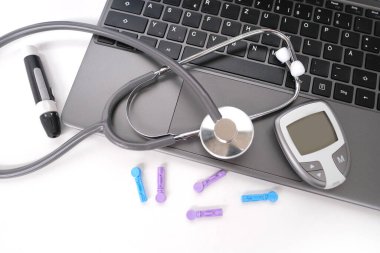 Tıbbi stetoskop, yedek iğneler, glukometre, beyaz arka planda dizüstü bilgisayar klavyesi, evdeki kan şekerini ölçmek için ekipman
