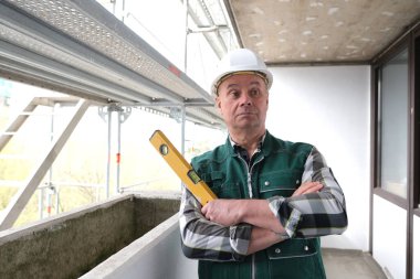 Koruyucu beyaz kasklı ve işçi üniformalı yaşlı inşaatçı inşaat ve onarım için inşaat alanında duruyor. İnşaat mühendisliği konsepti.