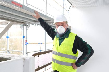 Erkek ustabaşı, beyaz şapkalı işçi, inşaat sahasında duruyor. Binaların, binaların, yapıların, iskelelerin tamiri kavramı...