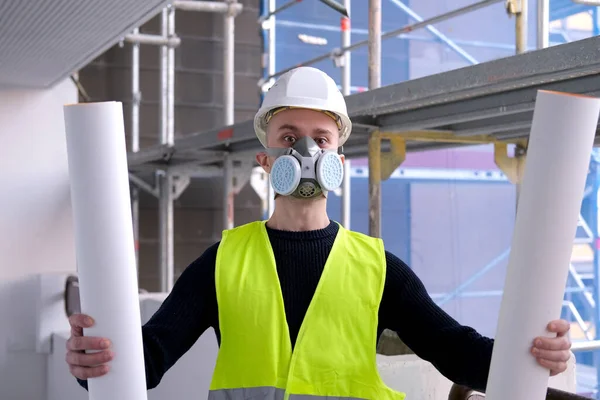 young male builder engineer, worker or architect in white hardhat and protective respirator during inspection in construction site, concept of monitoring repair of buildings, structures