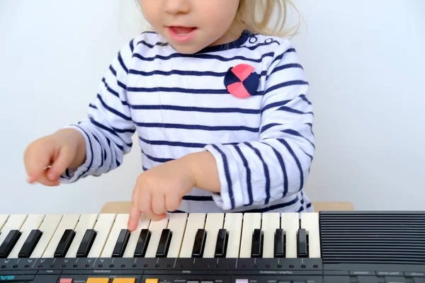 close-up of the hand of a small child, a 2-year-old girl with white hair on the keyboard of an electric piano, enjoys music, the concept of childhood, creative self-realization