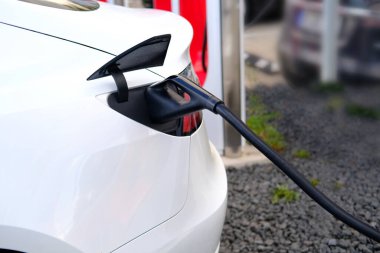 Beyaz yolcu elektrikli otomobili şarj istasyonundaki bataryayı yeniler, alternatif enerji geliştirme kavramı, elektrikli araçların üretimi, şehirlerin ekolojisi