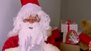 Geleneksel kırmızı sakallı Noel Baba süslemeli bir Noel ağacının yanında oturuyor, hediyelerle dolu kutular, mutlu yıllar diliyor, tebrik, mutlu noeller, mutlu noeller