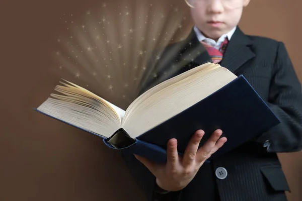 smart child 7-8 years old, kid in black school suit stands and reads thick tome, open paper book with magic glow and question marks, concept young child prodigy, back to school