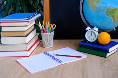 Beyaz alarmlı ofis masası, kitaplar, turuncu, renkli defterler, cam kalemler, tebeşir tahtası, dünya, beyaz alarm saati, eğitim konsepti, okula dönüş, bilgi günü.