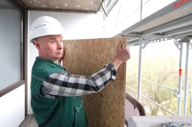 Beyaz kask korumalı inşaat malzemeleri ve üniformalı komik yaşlı müteahhit inşaat ve onarım için inşaat alanında çalışıyor.