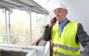 Tecrübeli bir inşaatçı, inşaat ekibi şefi, miğfer koruma mühendisi inşaat inşaatı için inşaat alanında telefonla konuşuyor, inşaat mühendisliği konsepti.