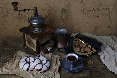 Gri bir fincanda kahve, ahşap bir masada çay tabağı, ceviz, eski el yapımı kahve öğütücüsü, jöleli iki çörek, kahve zamanı konsepti, retro tarzı.
