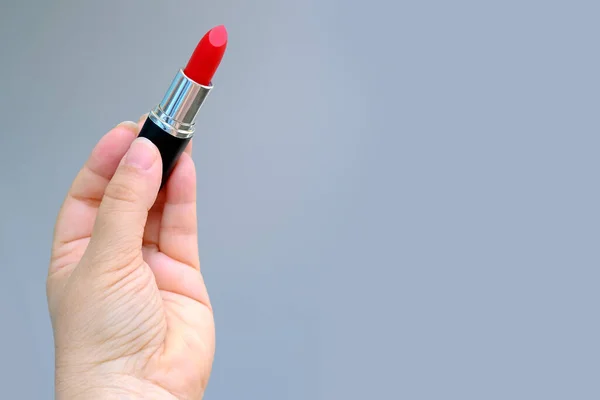 特写镜头中的女性手拿着一支灰色背景的新的亮红色口红管 想化妆 装饰化妆品的概念 女性的日常作息 — 图库照片
