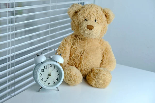 Witte Wekker Teddybeer Tegen Achtergrond Van Rolluiken Tafel Uur Concept — Stockfoto