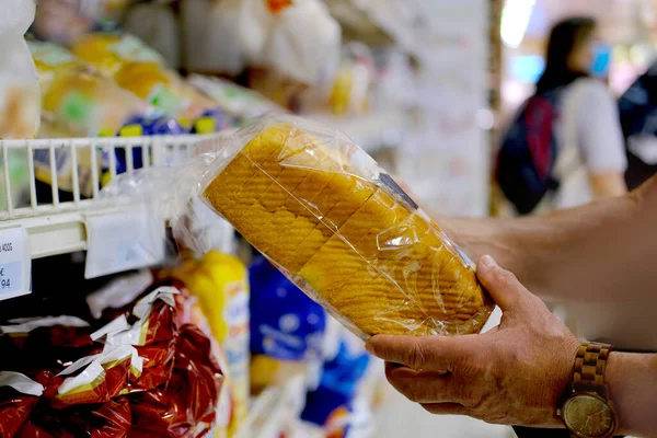 Mão Masculina Segura Pão Fundo Embaçado Uma Fileira Prateleiras Com — Fotografia de Stock