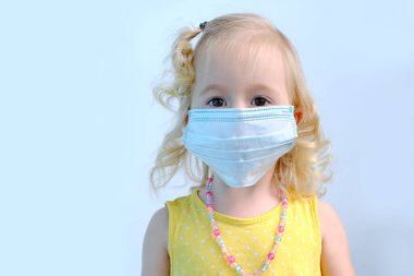 Koronavirüs covid-19, çocukluk kavramına karşı korunmak için küçük bir çocuğun yakın plan fotoğrafı, sarı yaz elbisesi içindeki iki yaşında sarışın bir kız, beyaz tıbbi maske.