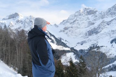Kameralı yaşlı bir adam, dağ yürüyüşçüsü kış manzarasına hayran, spor konsepti, sağlıklı yaşam tarzı, kış etkinliği, güzel kış doğal manzarası, kışın beyaz ormanda yürüyor.