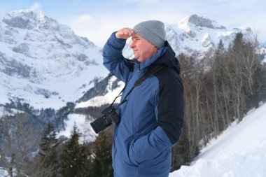 Kameralı yaşlı bir adam, dağ yürüyüşçüsü kış manzarasına hayran, spor konsepti, sağlıklı yaşam tarzı, kış etkinliği, güzel kış doğal manzarası, kışın beyaz ormanda yürüyor.