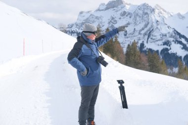 Kameralı yaşlı bir adam, dağ yürüyüşçüsü kış manzarasına hayran, spor konsepti, sağlıklı yaşam tarzı, kış etkinliği, güzel kış doğal manzarası, kışın beyaz ormanda yürüyor.