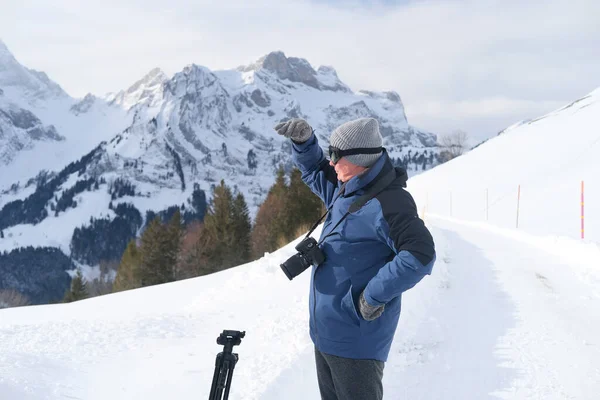 Kameralı yaşlı bir adam, dağ yürüyüşçüsü kış manzarasına hayran, spor konsepti, sağlıklı yaşam tarzı, kış etkinliği, güzel kış doğal manzarası, kışın beyaz ormanda yürüyor.