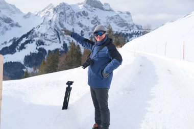 Kameralı yaşlı bir adam, dağ yürüyüşçüsü kış manzarasına hayran, spor konsepti, sağlıklı yaşam tarzı, kış etkinliği, güzel kış doğal manzarası, kışın beyaz ormanda yürüyor.