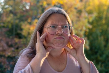 50 yaşında orta yaşlı bir kadın, insan kulağı çınlıyor, dinliyor, akustik işitme sistemi, işitme testi, koklear implant, yardımcı dinleme cihazı, sağlıklı yaşlanma, kaliteli olgun yaşam, sağlık kontrolü. 