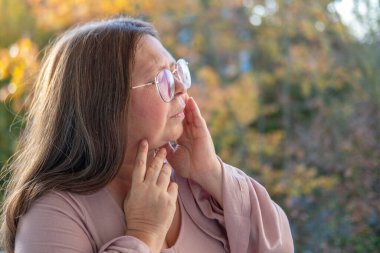 50 yaşında orta yaşlı bir kadın, insan kulağı çınlıyor, dinliyor, akustik işitme sistemi, işitme testi, koklear implant, yardımcı dinleme cihazı, sağlıklı yaşlanma, kaliteli olgun yaşam, sağlık kontrolü. 