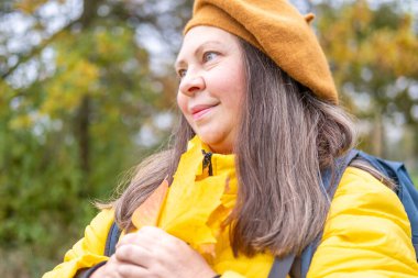 Düşen yapraklı mutlu olgun bir kadın, kadın elinde sarı bir yaprak, kafasında bere, parkta arka plan, orman sakin, zarif yaşlanma, hayat dolu yaşlanma, sağlıklı yaşam tarzı, altın yapraklar, sonbahar havası konsepti