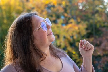 Neşeli, olgun bir kadın eğleniyor, komik bir yüz ifadesi yapıyor, neşeli hareketlerle komik bir resim yapıyor, garip bir ifade sergiliyor, açık havada kendiliğinden çekilen bir an.