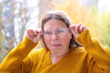 50 yaşında gözlük takan olgun bir kadın, kötü görüş, miyop sorunu, optik muayene, diopter hassasiyeti, gözlüklü bir kadın, doğru lens diopterleri, görüş sağlığı, duygusal portre, yaşlanma