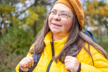 Mutlu orta yaşlı kadın, renkli sonbahar ormanlarında yürüyüş yapan olgun turist, doğa sever, sağlıklı yaşam tarzı, yaşlı kadınlar için çevre dostu aktiviteler.