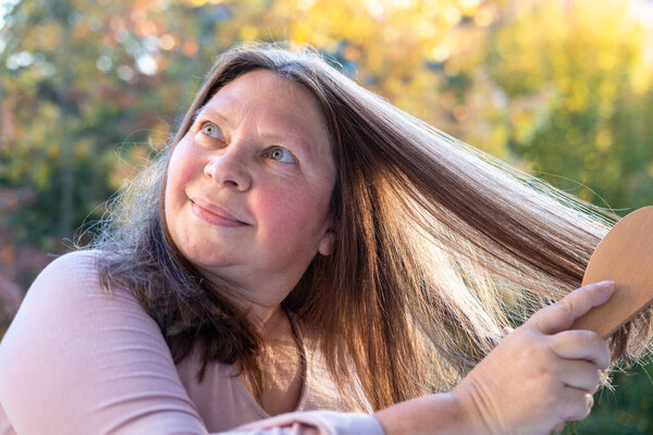 wooden comb, brush in female hand, woman combing long brown hair, tangles fallen hair wound on brush pins, concept hair loss, health, causes, treatment alopecia, hormonal imbalance