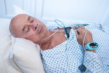 Karnına taşınabilir uyku cihazı takan yaşlı bir adam. Uyku ve karın bölgesinde sağlık izleme cihazı olan yaşlı bir erkek hasta. Sürekli takip için parmak ucu nabız oksimetresi.