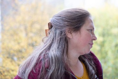 Sonbahar parkında düşünceli, nötr bir ifadeye sahip olgun bir kadın yüzü nötr duygulara sahip, gözlerinin etrafında kırışıklıklar, yumuşak doğal ışık, sakin ruh hali, mevsimsel portre konsepti