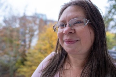 Sonbahar parkında düşünceli, nötr bir ifadeye sahip olgun bir kadın yüzü nötr duygulara sahip, gözlerinin etrafında kırışıklıklar, yumuşak doğal ışık, sakin ruh hali, mevsimsel portre konsepti