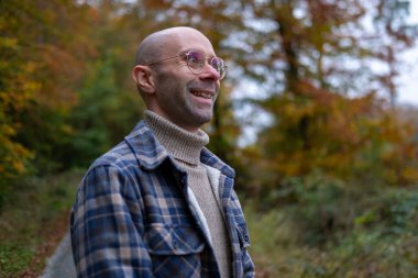 Yeşil orman parkında ekose gömlekli çekici bir genç adam. Moda ve doğal ortam, orman macerası, gündelik görünüş.