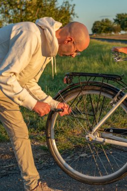 Bisikletçi Adam gün batımında bisiklet lastiğini şişiriyor, hobi seyahati, onarım, bisiklet yaşam tarzı, kırsal etkinlik, sağlıklı açık hava, insan ve doğa arasındaki bağlantı, kırsal yaşam