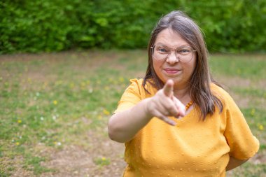 Stresli orta yaşlı kadın dışarıda negatif duygular sergiliyor. Çevresi yeşillik ve dingin çevreyle çevrili. Öfke ve gerilimle reaksiyon gösteriyor.