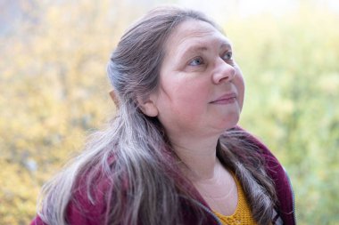 Sonbahar parkında düşünceli, nötr bir ifadeye sahip olgun bir kadın yüzü nötr duygulara sahip, gözlerinin etrafında kırışıklıklar, yumuşak doğal ışık, sakin ruh hali, mevsimsel portre konsepti