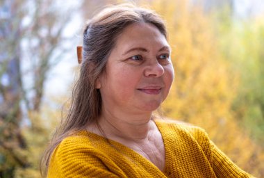 Sonbahar parkında düşünceli, nötr bir ifadeye sahip olgun bir kadın yüzü nötr duygulara sahip, gözlerinin etrafında kırışıklıklar, yumuşak doğal ışık, sakin ruh hali, mevsimsel portre konsepti