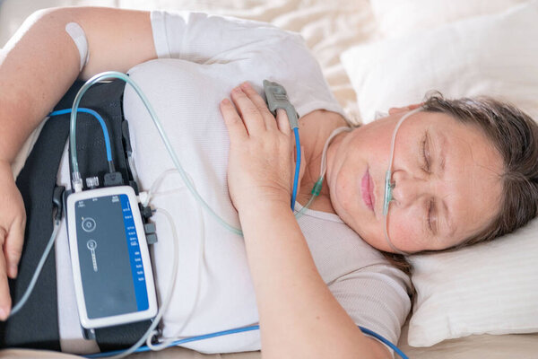 Женщина носит портативный датчик сна на брюшной полости, пациентка с устройством мониторинга сна и здоровья на брюшной полости и кончика пальца пульсометр для непрерывного отслеживания, храпа проблемы
