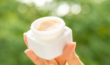 Elleri kavanozu pürüzsüz, doğal görünümlü krem, nazik cilt bakımını ve bütünsel güzellik rutinlerini sembolize eden cilt ürünleri, hafif sunulan cilt ürünleri, saflık ve organik bileşenleri vurguluyor. 