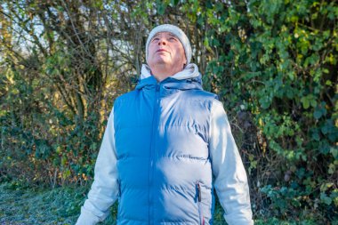 Sonbahar parkının arka planında donuk bir yolda duran mavi yelekli yaşlı adamı kapatın, aktif son sınıf öğrencisinin portresi, sade neşe, huzur ve mutluluk, sağlıklı yaşlanan günlük bağ ortamı