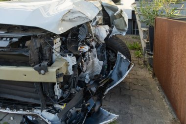 Çarpışmadan sonra ağır hasar gören beyaz araba, buruşuk kaput ve açık motor bölmesi, yapısal deformasyon ve mekanik maruziyet, kaza mahalli, tampon ve çamurluk, güvenlik ve sigorta kavramı