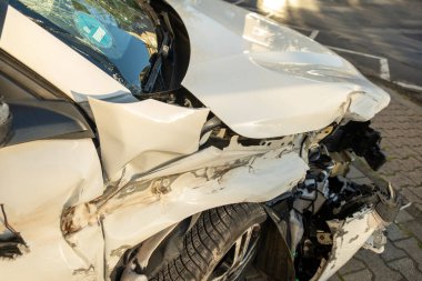 Çarpışmadan sonra ağır hasar gören beyaz araba, buruşuk kaput ve açık motor bölmesi, yapısal deformasyon ve mekanik maruziyet, kaza mahalli, tampon ve çamurluk, güvenlik ve sigorta kavramı