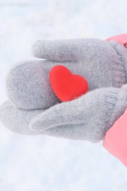 Pembe ceketli bir kız elinde aşkın sembolü ellerinde gri yün eldivenler, kış arkaplanı ve beyaz kar, günah çıkarma konsepti, sevgililer günü konsepti.