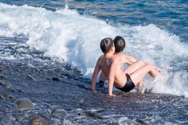 İki küçük çocuk, iki genç erkek çocuk denize dalıp oynuyorlar güneşli bir yaz gününde okyanus dalgaları, aile aktiviteleri, su maceraları çocuklarda merak ve çevreye olan sevgiyi arttırıyor.