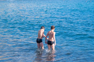 İki küçük çocuk, iki genç erkek çocuk denize dalıp oynuyorlar güneşli bir yaz gününde okyanus dalgaları, aile aktiviteleri, su maceraları çocuklarda merak ve çevreye olan sevgiyi arttırıyor.